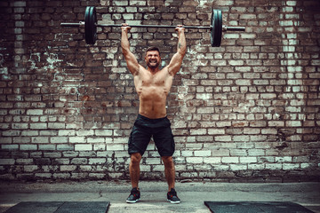 Muscular fitness man doing deadlift a barbell over his head in outdoor, street gym. Functional...
