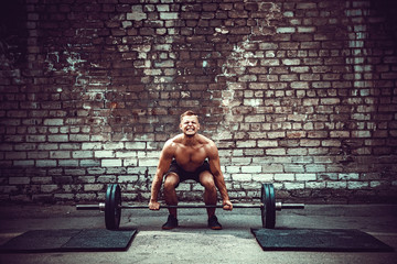 Muscular fitness man doing deadlift a barbell over his head in outdoor, street gym. Functional...