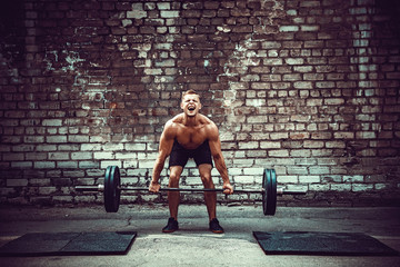Muscular fitness man doing deadlift a barbell over his head in outdoor, street gym. Functional...