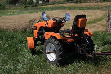 Tractor on the field/ The orange minitractor works in the field. Agricultural multifunction machine with a trailer collects the harvest.