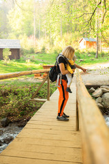 Happy mother with little boy travelling in backpack. Hiking adventure with child on spring in mountains. Vacations journey with infant carried in front to the waterfall Shipot, Carpathians, Ukraine