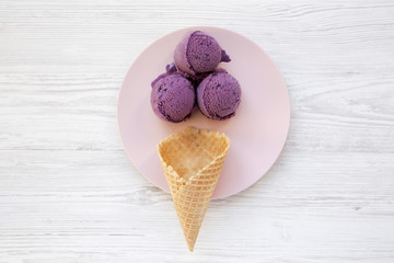 Top view, blueberry ice cream balls with icecream cone on a pink plate. White wooden background. From above, flat lay.