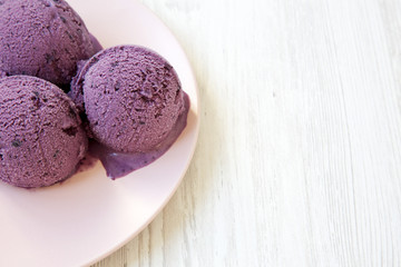 Blueberry ice cream balls on a pink plate on white wooden surface, side view. Closeup. Copy space.