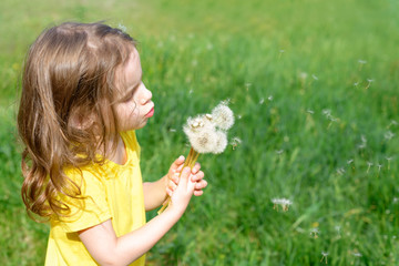 Beautiful child with dandelion flower in spring park. Happy kid having fun outdoors.