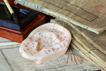Ear model and needle for ear acupuncture with ancient medicine books at the background...