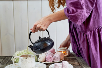 The red-haired girl in a purple dress pours tea in a Cup, the table is set in the air. Marshmallow.