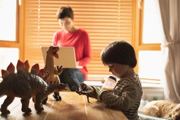 Boy playing toys while mother using laptop