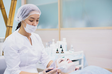 The doctor-cosmetologist makes a procedure of ultrasound facial cleaning of the skin of a...