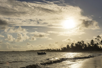 Obraz premium Boat by the sea at sunset with palm trees in the background.