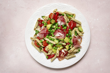 Delicious whole wheat pasta penne with vegetables ( tomato, zucchini, grilled bell pepper, green pea ) and prosciutto.Top view with copy space.