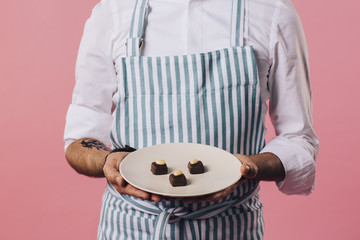 Midsection of man in apron holding plate with pralines
