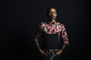 Portrait of a stylish cook with tattoos with hands on waist, isolated on blackbackground