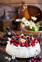 Delicious Pavlova meringue cake decorated with fresh raspberries and cherries on rustic background