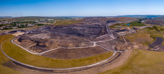 Aerial drone view of a huge opencast coal mine cut into a rural hilly area