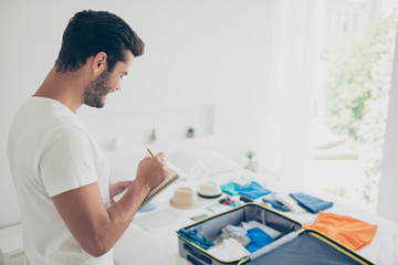It's better to make a list! Joyful brunet man in a white T-shirt writes down what to take with him on a trip