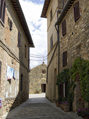 Fototapeta na wymiar ancient church seen between old stone buildings in Monteriggioni, Italy under bright blue clouded sky