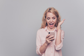 Young lovely attractive caucasian curly-haired cheerful charming gorgeous excited woman wearing formal wear, reading notification in smartphone.  Isolated over grey background, copy space