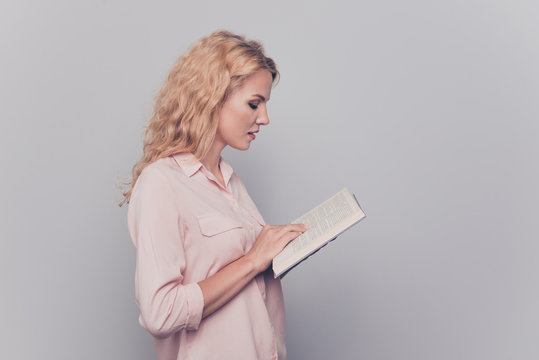 Young lovely attractive caucasian curly-haired charming gorgeous smiling woman wearing formal wear, reading book. Isolated over grey background, side view