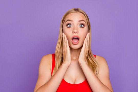 Portrait of attractive shocked blonde gorgeous girl wearing red swim suit holding palms near cheeks, surprised expression. Isolated over violet pastel background