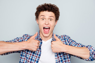 Close up portrait of excited young man with opened mouth giving thumbs-up isolated on light gray background
