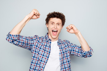 Close up portrait of surprised young guy who celebrates the victory hold hands in fist and screaming loud for joy isolated on light gray background