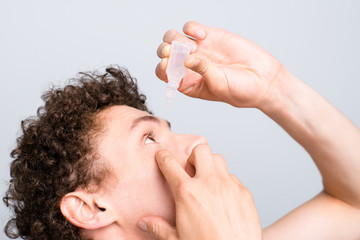 Crop photo of young man burying his eyes with drops isolated on light gray background