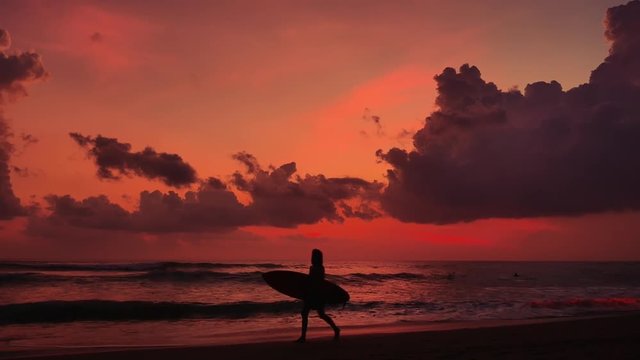 Surfer with surf board walking on beach at sunset
