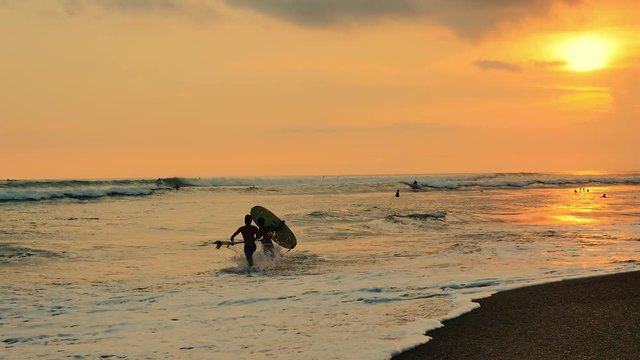 Beach and coastline of Bali island at sunset. Surfers ride surboards slow motion video of summer water sport activity