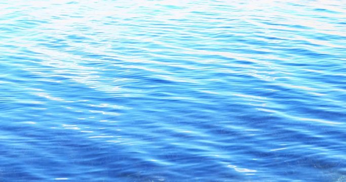 Soft and smooth blue water surface texture tranquil slow motion background. Gentle waves and calm glittering ripples at sunny day 4K nature video