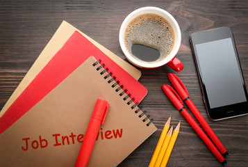 Notebook with text JOB INTERVIEW, mobile phone and stationery on table
