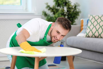 Young man cleaning table with rag indoors