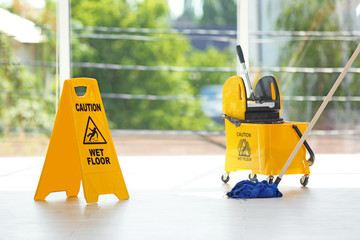 Safety sign with phrase Caution wet floor and mop bucket, indoors. Cleaning service