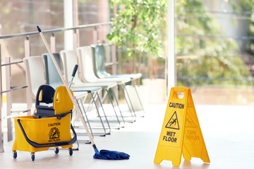 Safety sign with phrase Caution wet floor and mop bucket, indoors. Cleaning service