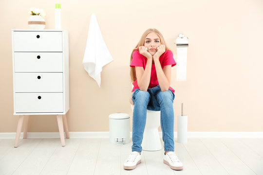 Young woman sitting on toilet bowl at home
