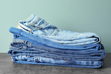 Stack of jeans on table against color background