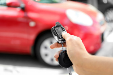Young woman pushing button on remote control of car alarm system, outdoors