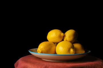 Plate with whole lemons on table against dark background