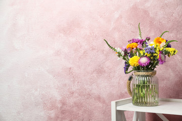 Vase with wild flowers on table against color background