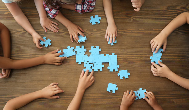 Top view of little children playing puzzle together at table, focus on hands. Unity concept