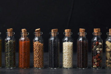 Glass bottles with different spices on table against black background