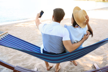 Young couple taking selfie in hammock at seaside