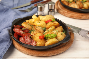 Pan with fried potatoes and sausages on wooden table