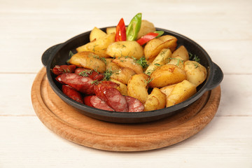 Pan with fried potatoes and sausages on wooden table