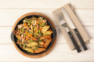 Pan with fried potatoes, meat and vegetables on wooden table, top view