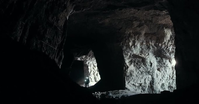 Young people in helmets walking through the dark deepest cave