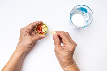 Senior woman's hands holding Vitamin C pills and Antianemia pills in bottle with polka dot glass of water, Healthcare and medical concept