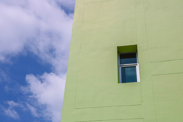 A window on a light green building with a sky background.