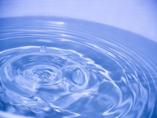 Naklejka na ściany i meble Close up blue water drop falling into water making a reflection concentric circles. Blue wave.