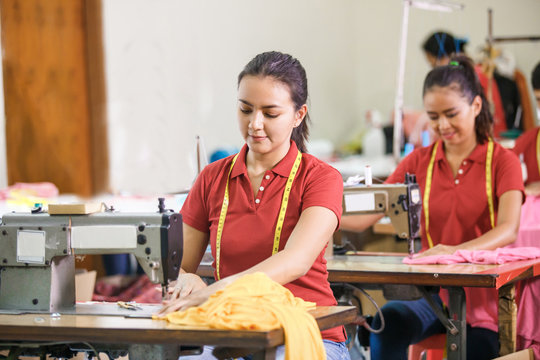 Asian Seamstress In Garment Factory Sewing With Industrial Sewin