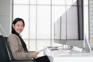 Businesswoman sitting in front of new computer in modern office, smiling and looking at camera. Concept for working woman lifestyle.
